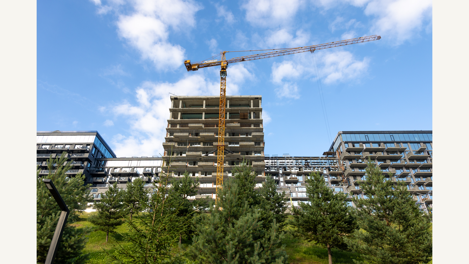 Illustration of a wide construction site with a tower crane and modern apartment buildings, showing active urban residential development.